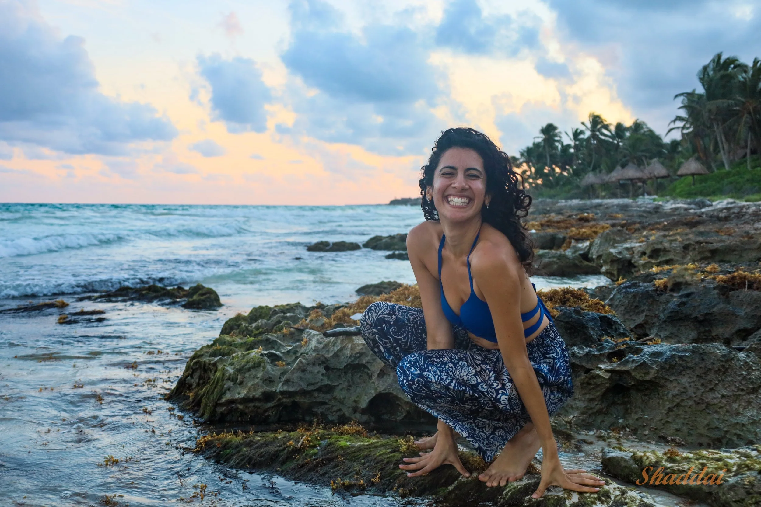 Haneen Khan sitting on a rocky beach shoreline, smiling